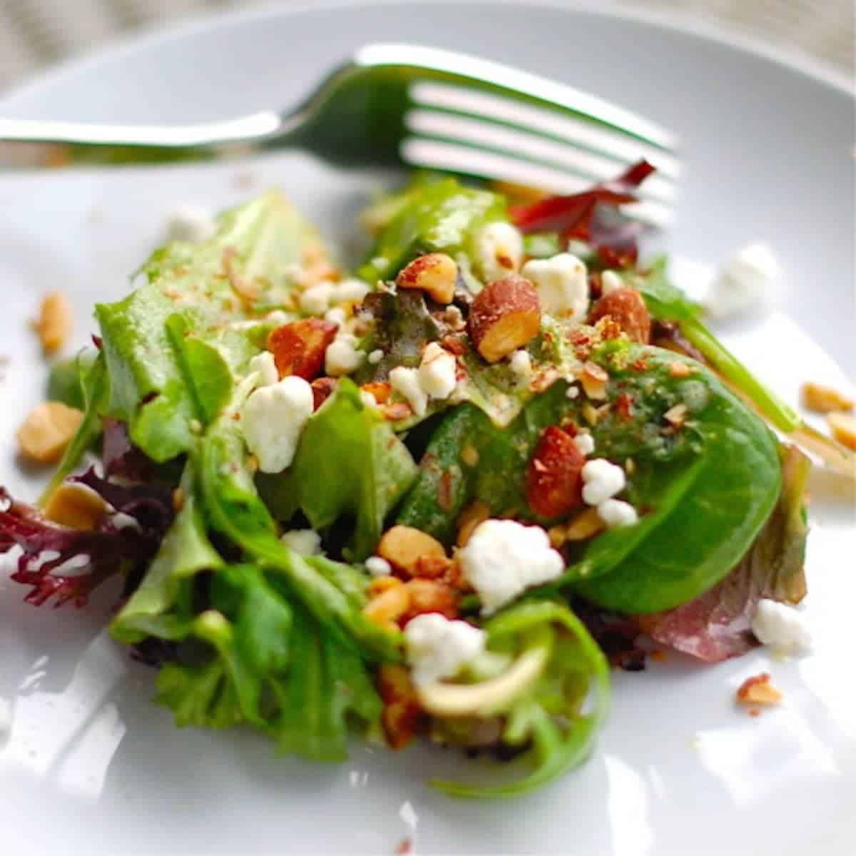 Smoked almond and goat cheese salad on a white plate with a fork.