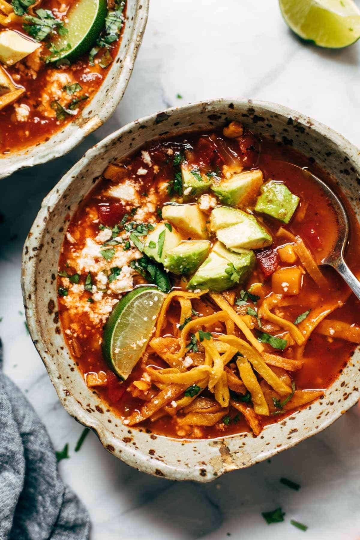 Sweet potato tortilla soup in a bowl with avocado and tortillas on top.