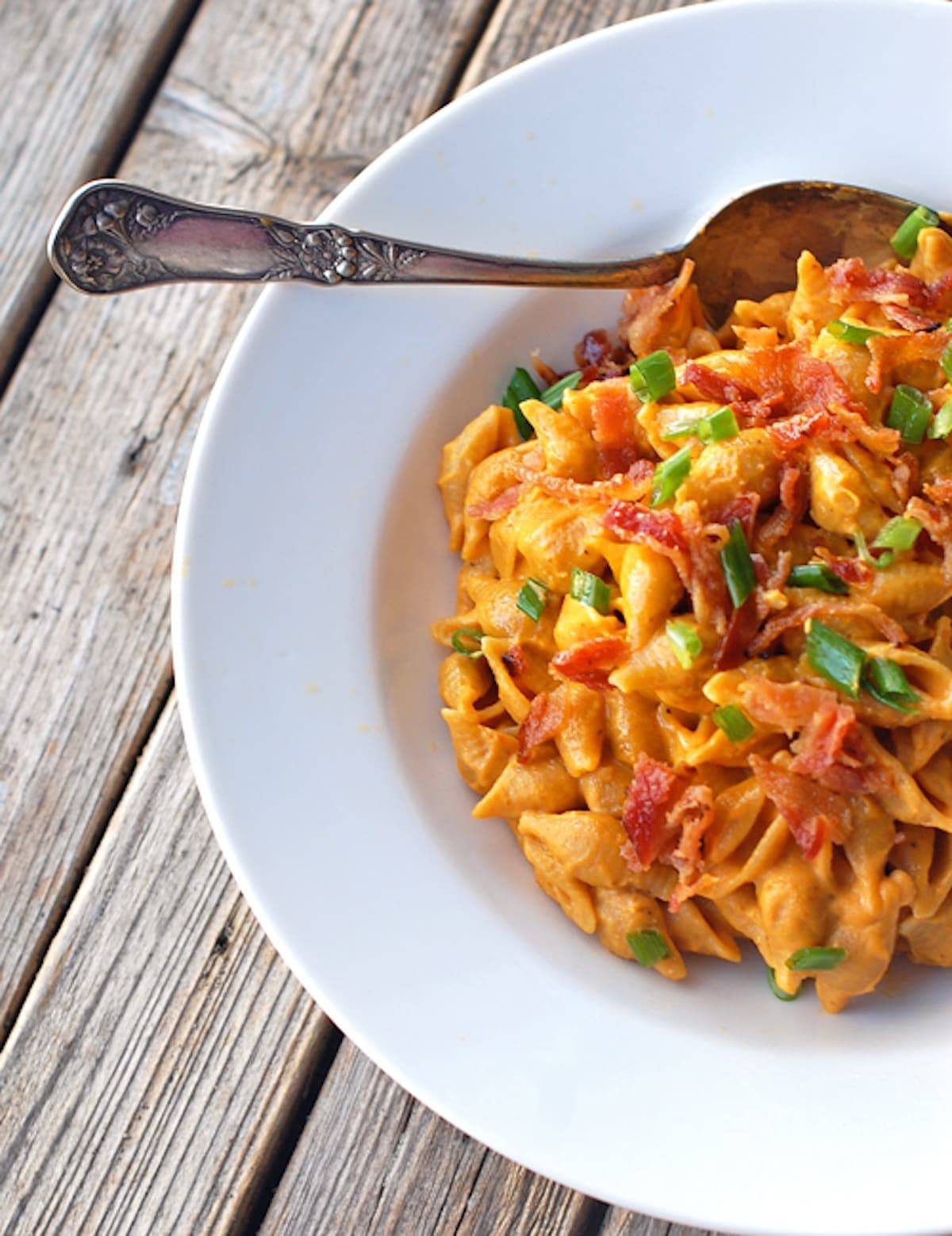 Bacon and pumpkin pasta with a creamy pumpkin sauce, whole wheat pasta shells, and crumbled bacon in a bowl with a spoon.